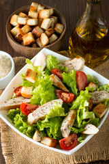 Fresh salad made of tomato, ruccola, chicken breast, eggs, arugula, crackers and spices. Caesar salad in a white, transparent bowl on wooden background