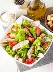 Fresh salad made of tomato, ruccola, chicken breast, eggs, arugula, crackers and spices. Caesar salad in a white, transparent bowl on wooden background