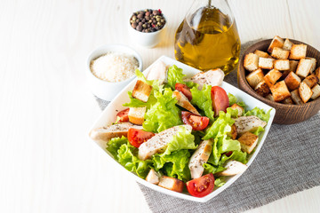 Fresh salad made of tomato, ruccola, chicken breast, eggs, arugula, crackers and spices. Caesar salad in a white, transparent bowl on wooden background