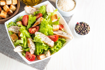 Fresh salad made of tomato, ruccola, chicken breast, eggs, arugula, crackers and spices. Caesar salad in a white, transparent bowl on wooden background