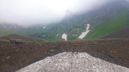 Obraz premium On the slope of a high mountain with a green slope and a top in clouds and fog. Sports and tourist base in the mountains. Krasnaya Polyana, Sochi, Russia.