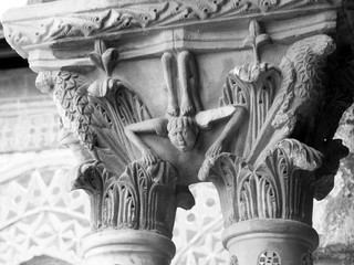Narrative Capital of a column from St Mary Cathedral Basilica in the cloister of Monreale Basilica in Sicily.  An acrobat between acanthus leaves is carved in a marble Corinthian capital. 