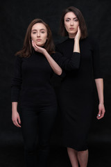 Concept portrait of two stylish brunette sisters on a black background in various poses. Fashionable photo of two beautiful girls with dark hair