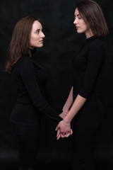 Concept portrait of two stylish brunette sisters on a black background in various poses. Fashionable photo of two beautiful girls with dark hair