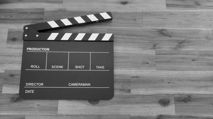 Clapper board or movie slate use in video production or film and cinema industry. It's black color on wood background with flare light.