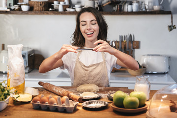 Cheerful young woman wearing apron preparing dough