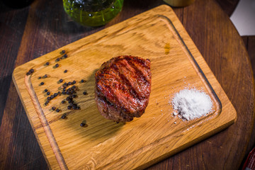 Grilled pork rib chop steak in a clay plate with oil, mustard, salt and rosemary is an old wooden table.