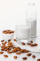 vegan fresh almond milk in bottle and glass near nuts in bowl isolated on white