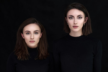 Concept portrait of two stylish brunette sisters on a black background in various poses. Fashionable photo of two beautiful girls with dark hair