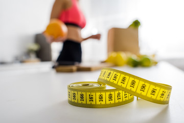 selective focus of yellow measuring tape near woman holding orange in kitchen
