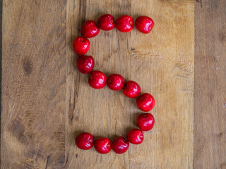  cherry on wooden background as a letter