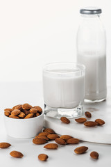almond milk in bottle and glass near nuts in bowl isolated on white