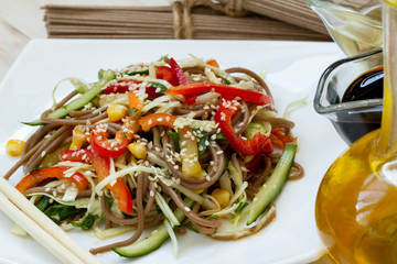 Japanese soba salad with vegetables and sesame close-up on a plate on the table. noodles salad. buckwheat noodle with vegetables. vegetarian Asian food horizontal top view from above. Healthy food.