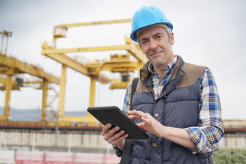 Mature construction worker inspecting work sight with tablet