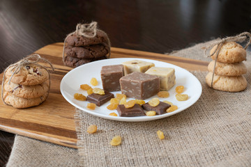 Homemade cookies,  halva , raisins and slices of milk chocolate on white plate . 