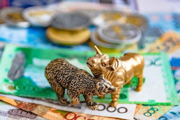 Bronze figures of a bull and a bear on the background of paper money and metal coins. Blur background and perspective. Concept and symbol of stock exchange and stock trading.
