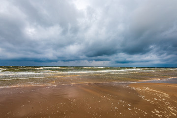 empty sea beach before storm with dramatic clouds and shadows from trees on the sand