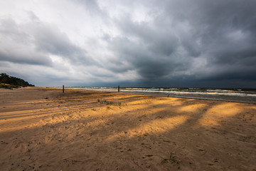 empty sea beach before storm with dramatic clouds and shadows from trees on the sand