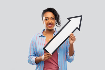 direction and people concept - happy african american young woman holding big white thick arrow showing to north east over grey background