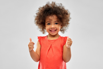 childhood, gesture and people concept - happy little african american girl showing thumbs up over grey background