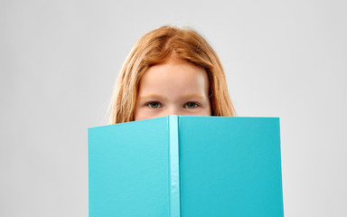 childhood and people concept - smiling red haired girl reading book over grey background