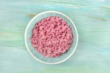 Obraz na płótnie Canvas A bowl of pink Himalayan sea salt, shot from the top on a teal blue background with a place for text