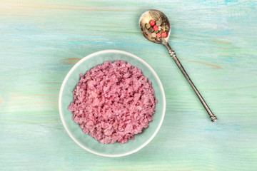 Obraz na płótnie Canvas A bowl of pink Himalayan sea salt with a mix of peppercorns, shot from above on a teal blue background with copy space