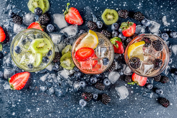 Fototapeta na wymiar Summer fruits and berry cold cocktail, Lemonade, infused water with blueberries, strawberries, blackberries, kiwi. lemon. Dark blue concrete background copy space