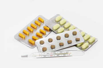 multi-colored yellow orange brown pills and a temperature thermometer on a white background