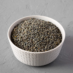 Dry green french lentils in a bowl  over gray background, low angle view. Close-up.