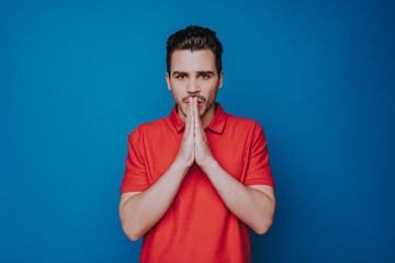Waist up of handsome unshaven man praying isolated on blue wall