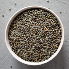 Dry green french lentils in a bowl over gray background, top view. Overhead, from above, flat lay.