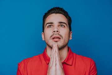 Close up of handsome unshaven man praying against blue background