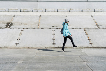 Profile view: a girl in a blue jacket is hopping on a concrete surface.