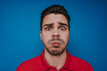 Portrait of surprised Caucasian man with grimacing face against blue background