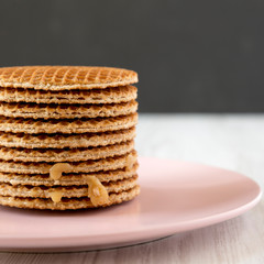 Stack of homemade Dutch stroopwafels with honey-caramel filling on pink plate, side view. Close-up.