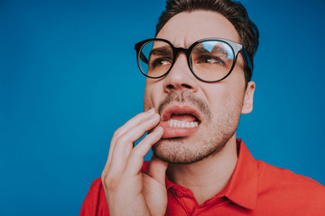 Close up of pensive upset guy in glasses on blue background