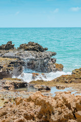 Fototapeta na wymiar Beach rocks, sea water hitting the rocks on the bay. Pointed spongy rocks. Set of rocks near the sea at Praia de Coqueirinho beach, Brazilian northeast beach. Costa do Conde, Conde PB Brazil.