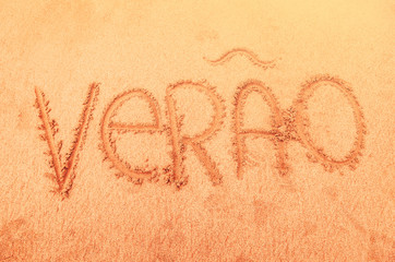 Word 'summer' written in portuguese (verao) on the beach sand. Summer background.