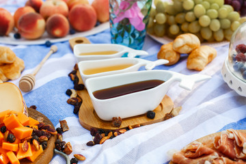 set of three white sauceboats with sweet honey on wooden tray at picnic food lay out background