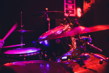 Drummer with a drumsticks in his hands playing on drum set on stage on the black background.