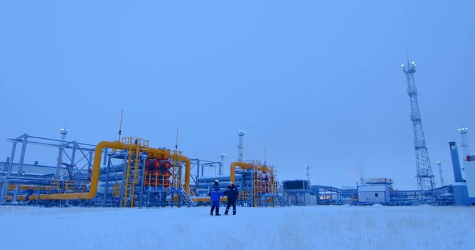 Workers in the gas and oil industries meet and greet each other against the backdrop of oil and gas pipelines. Cold winter outside, everywhere there is snow