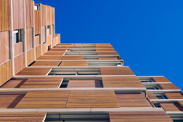 View from the floor of the facade of a modern building clad in ecological wood over clean blue sky,...