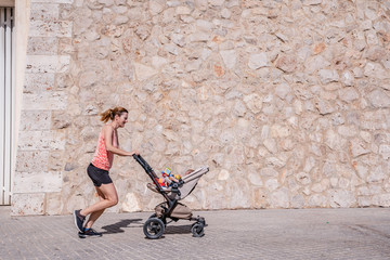 Young mother running with the stroller of her baby to stay in shape after childbirth.