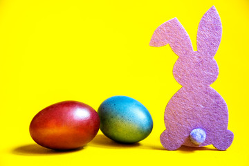 Lilac rabbit and easter eggs on a yellow background.