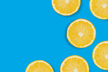 Obraz premium Scattered circles slices of fresh ripe oranges with pulp and peel on blue table on kitchen with copy space for your text. Top view. Concept of prepare of vegetarian food