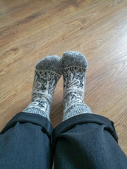 Women's legs with rolled-up pants in warm wool socks white with black pattern, standing on the wooden floor