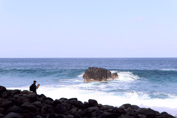 Blue gushing ocean with waves and white foam. Silhouette of a man in a distance. Cropped shot, horizontal, a lot of free space for text. The concept of nature and travel.