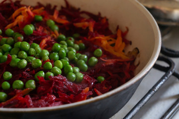 Green peas, beets and carrots stew in a frying pan