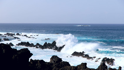 A view from the shore of the volcanic rocks in the ocean off the coast of the island of Madeira. The storming ocean. A cropped shot, horizontal, plenty of free space for text, without people